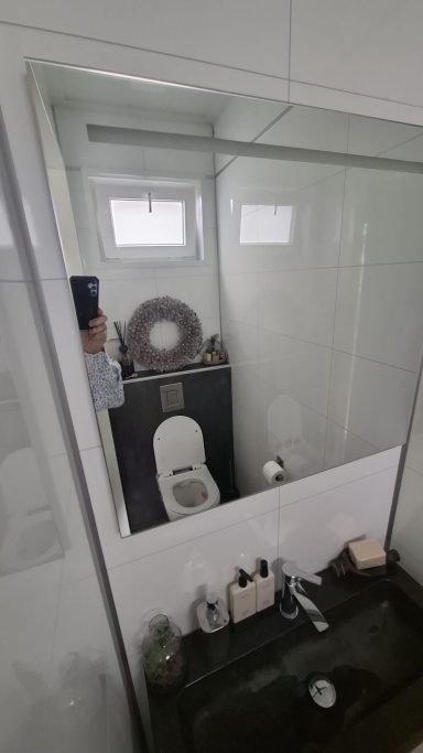 Toilet in een moderne badkamer met een spiegel en enkele toiletaccessoires.